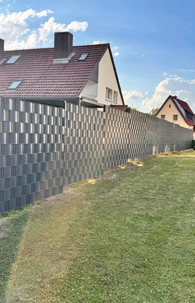Blickdichter Zaun mit anthrazitfarbenen Sichtschutzstreifen vor einem Wohnhaus